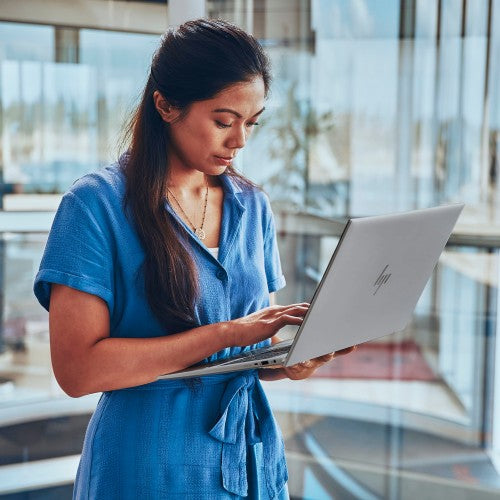 Woman in blue dress using a slim grey HP ZBook Firefly G11 laptop in a bright modern office.