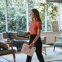 Woman holding a blue HP Elite Dragonfly laptop in one hand and the laptop screen in the other in a bright living room with.