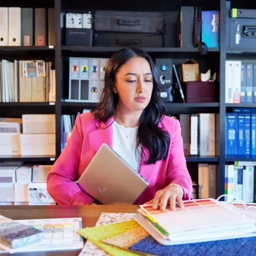 Grey HP ZBook Firefly G11 laptop held by woman in pink blazer at desk with color swatches.
