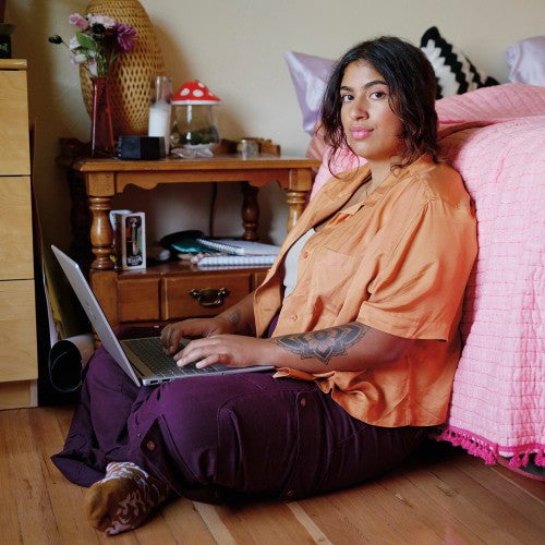 Silver HP 15.6-inch laptop open on lap of woman sitting on wooden floor against pink bedspread.